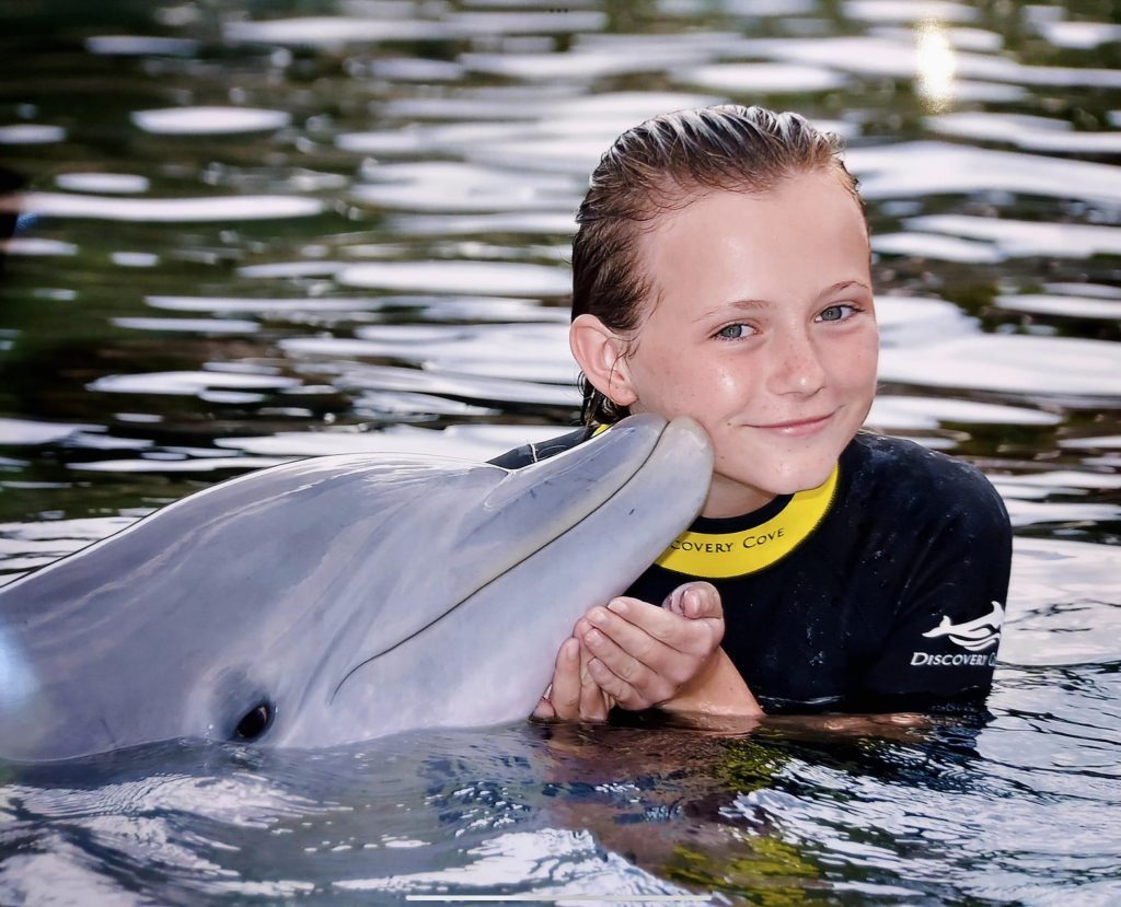 Day kissing a dolphin at Discovery Cove in Orlando, Florida, surrounded by crystal-clear water and lush tropical scenery.