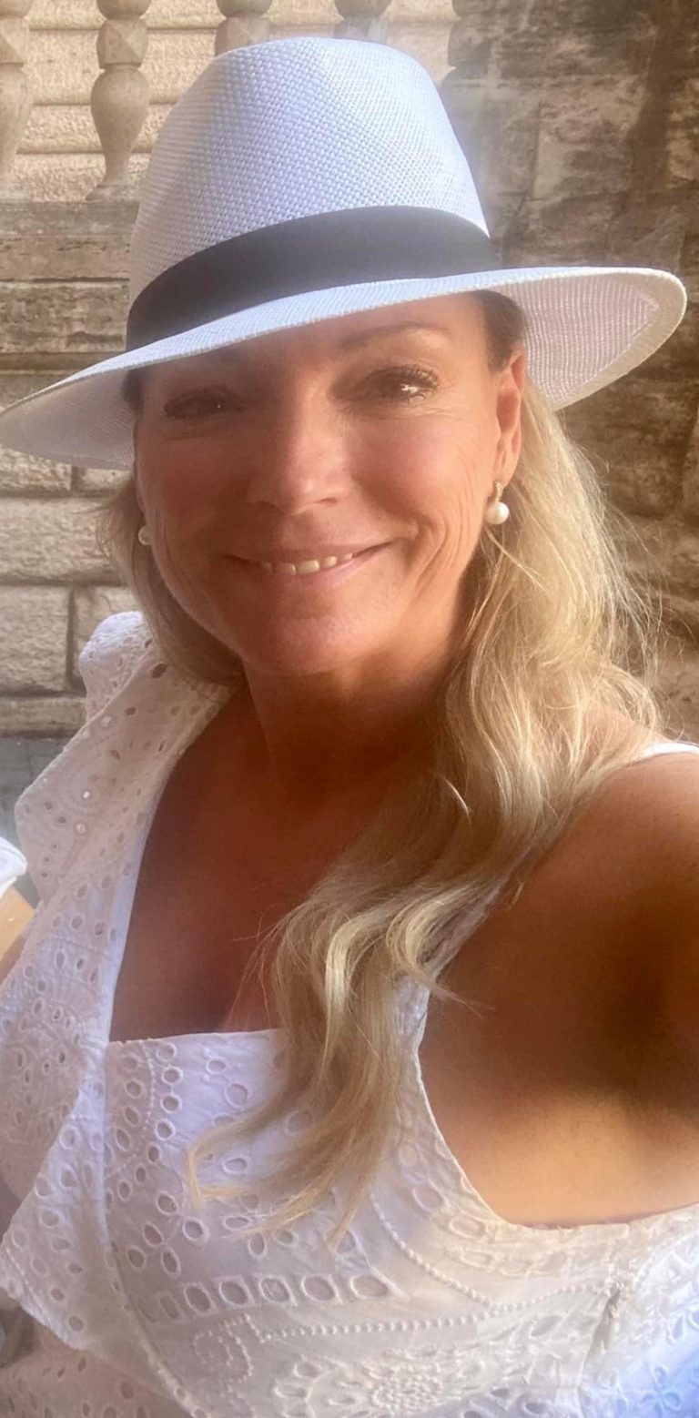 A woman dressed in white summer attire, wearing a white hat, enjoying a sunny day outdoors.