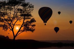 Four hot air balloons at sunset with mountains in the background.