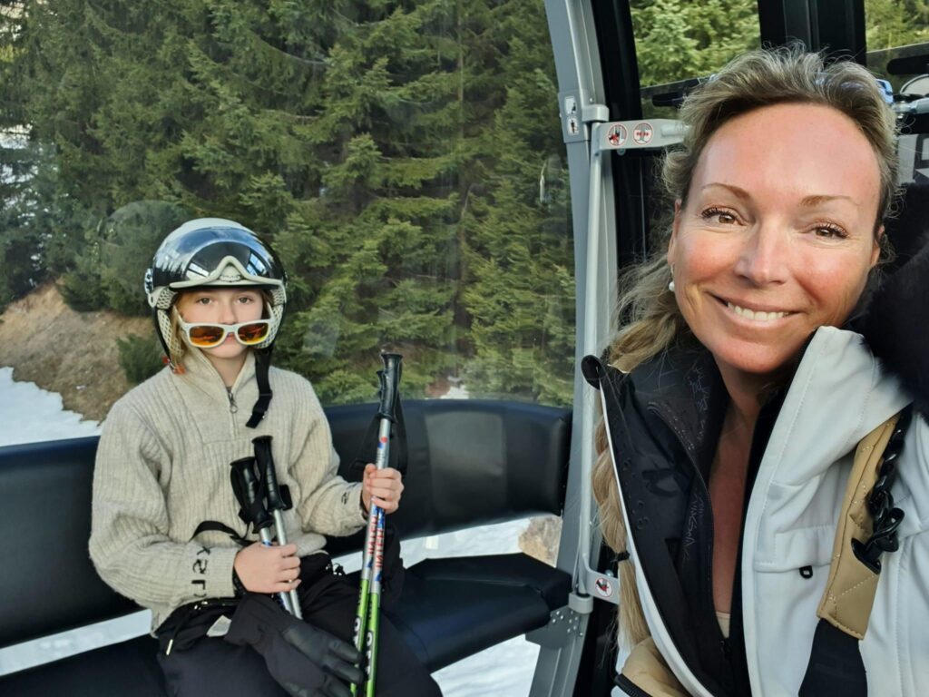 A mother and daughter sitting together in a gondola, dressed in ski gear, ready to hit the slopes and enjoy a day of skiing.