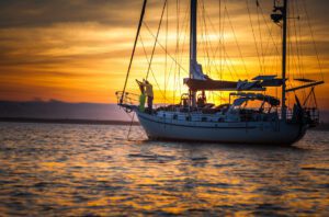 A sailboat gliding on calm waters during a breathtaking sunset, with vibrant orange and pink hues reflecting on the sea