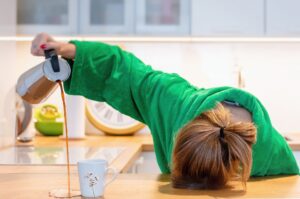 A fatigued woman rests her head on the kitchen counter while pouring coffee, reflecting the exhaustion of perimenopause.