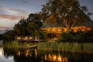 Luxury safari lodge glowing at dusk beside a quiet lake in Akagera National Park, Rwanda